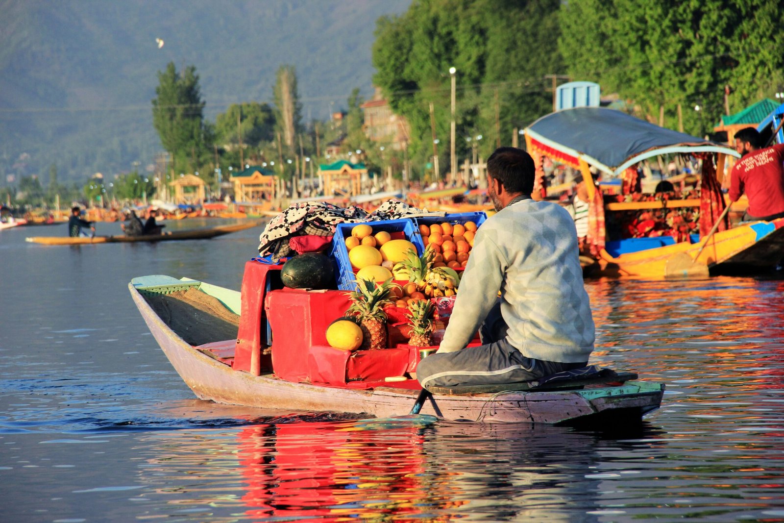 man sitting on boat selling different fruits