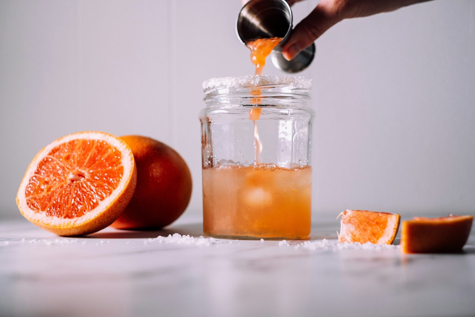 person pours liquid on jar near orange fruits